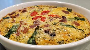 Eine weiße Schüssel mit einer gebackenen Speise, darunter Spinat, rote Paprika und Speck.