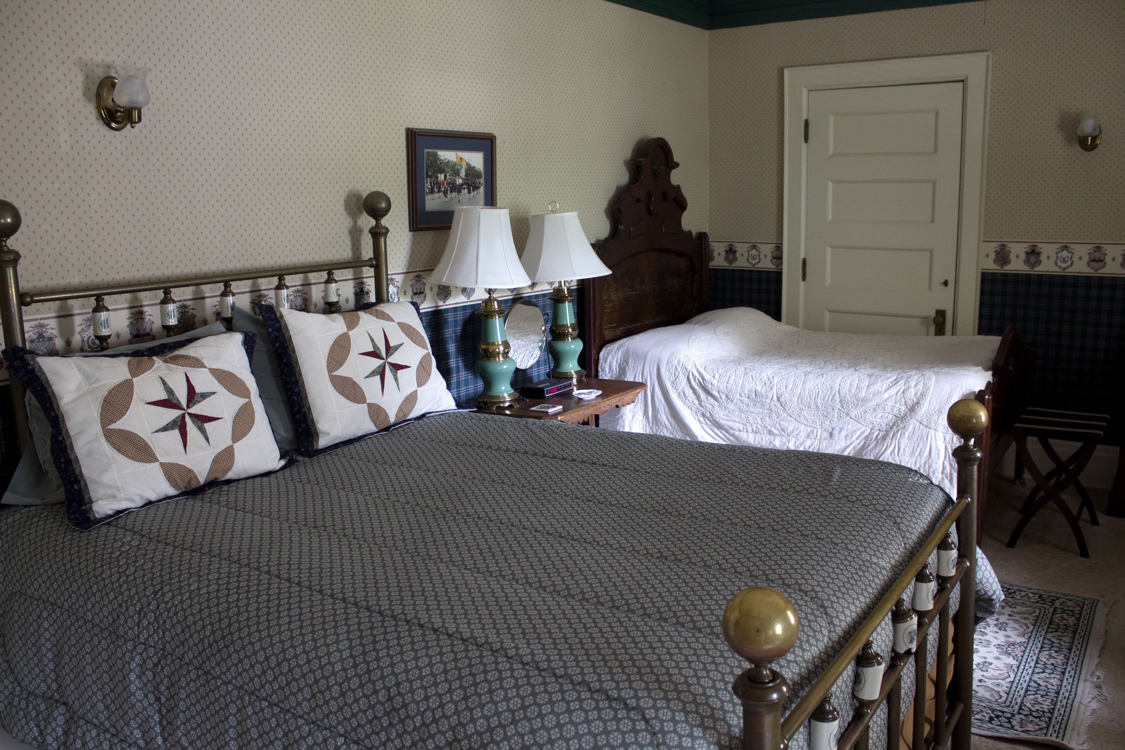 Uma cama de casal com colcha estampada, duas luminárias de cabeceira, um painel de madeira na cabeceira e um quadro na parede.