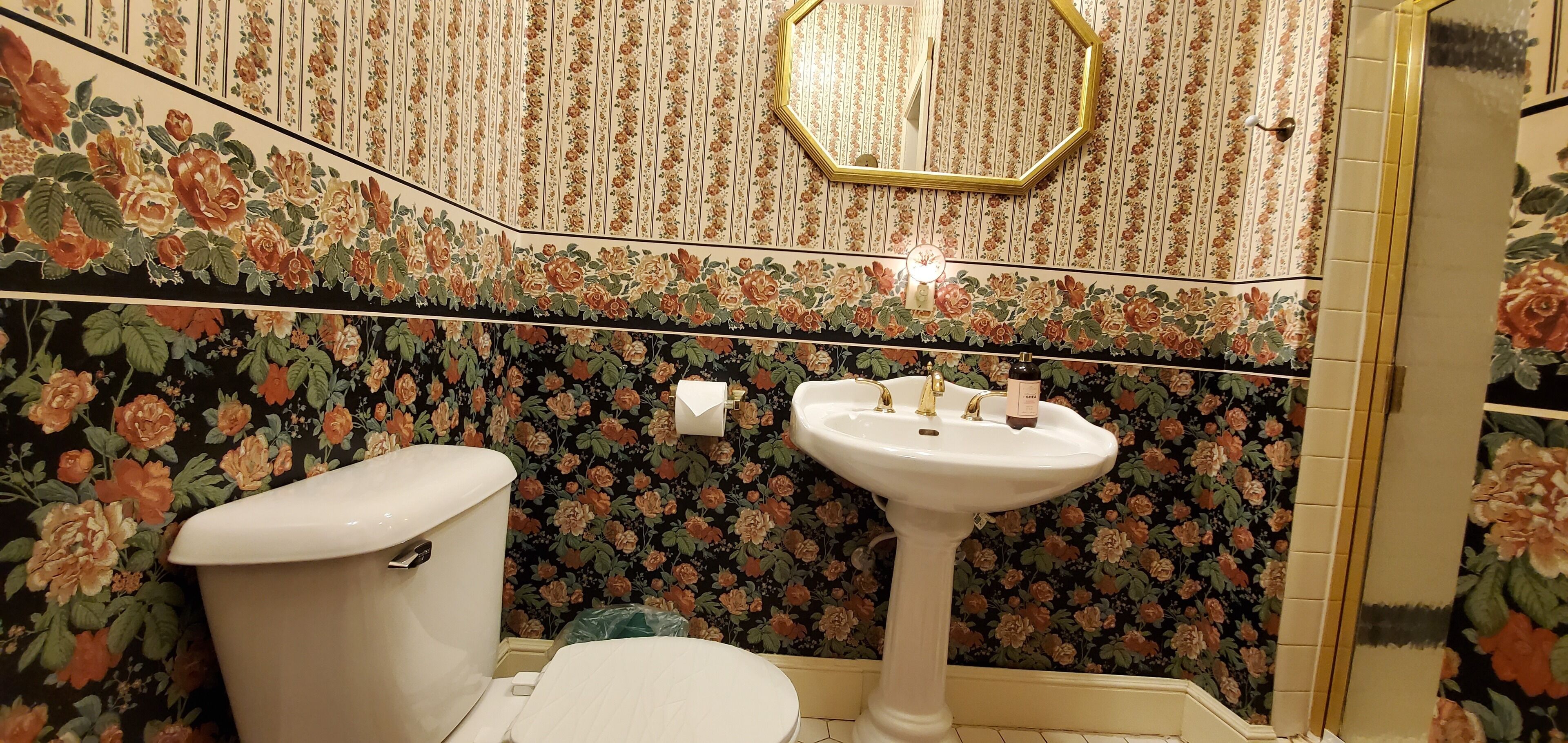 A bathroom with a toilet, sink, and mirror. The walls are decorated with floral wallpaper.