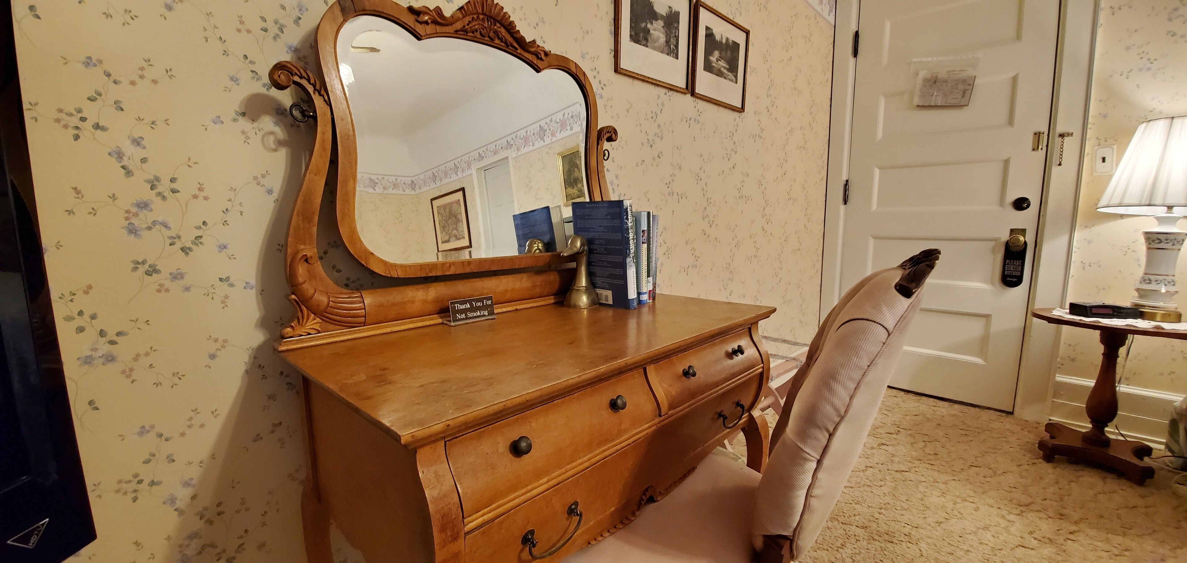 Un aparador de madera con espejo, una silla y una mesita de noche con lámpara.