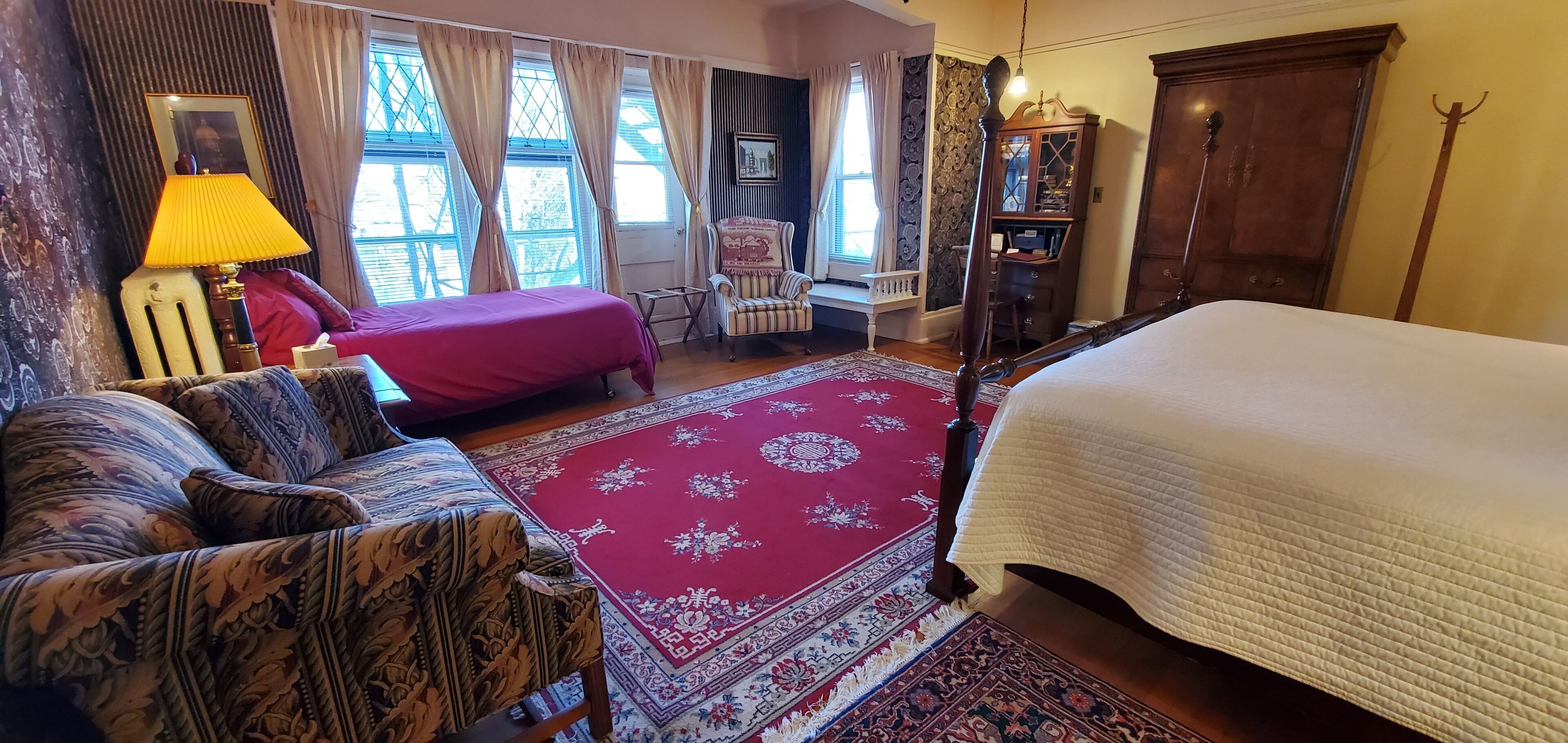 A traditional room with a large bed, a sofa, a chair, and a wooden cabinet.