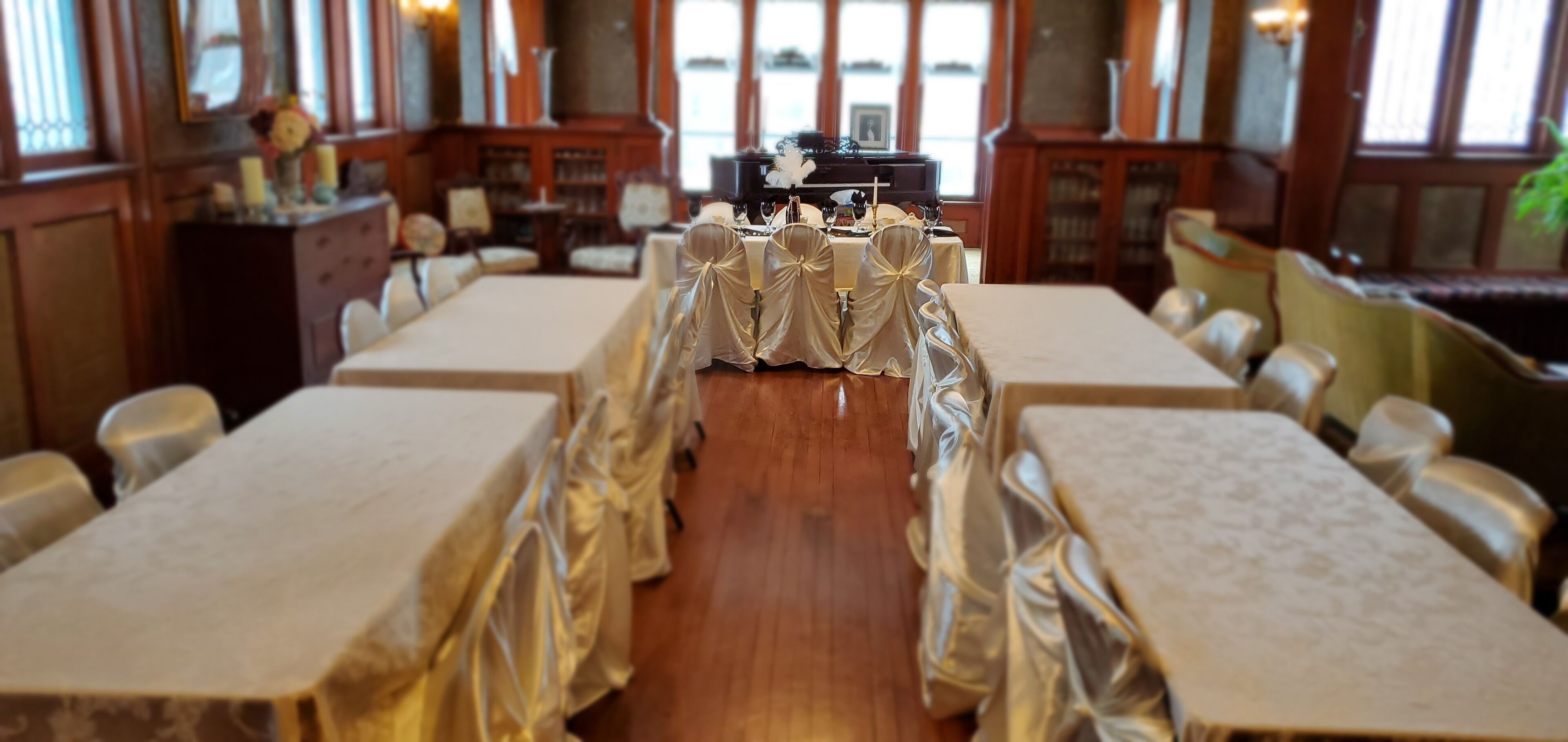 A banquet hall with long tables covered in white tablecloths and chairs draped with white cloths.