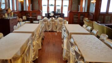 A banquet hall with long tables covered in white tablecloths and chairs draped with white cloths.