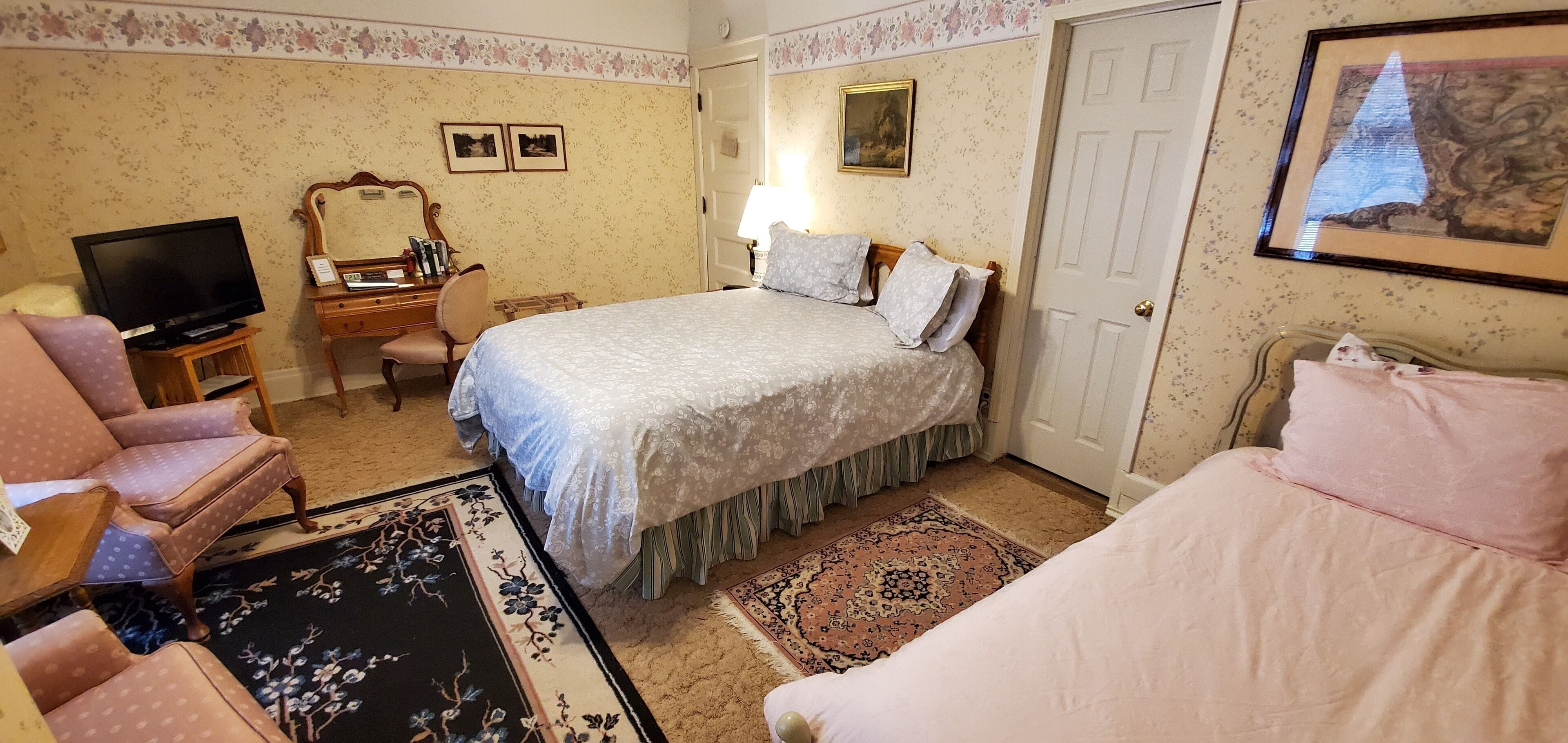 A hotel room with a bed, a chair, a desk with a television, and a lamp.