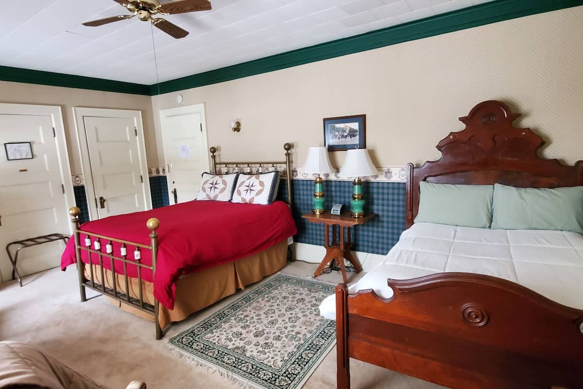 A bedroom with two beds, a ceiling fan, a bedside table with lamps, and a patterned rug.