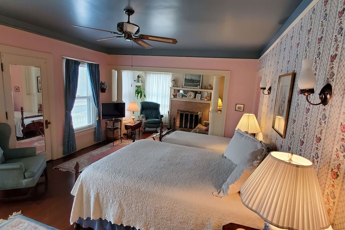 A bedroom with a bed, a chair, a desk, a television, and a fireplace.