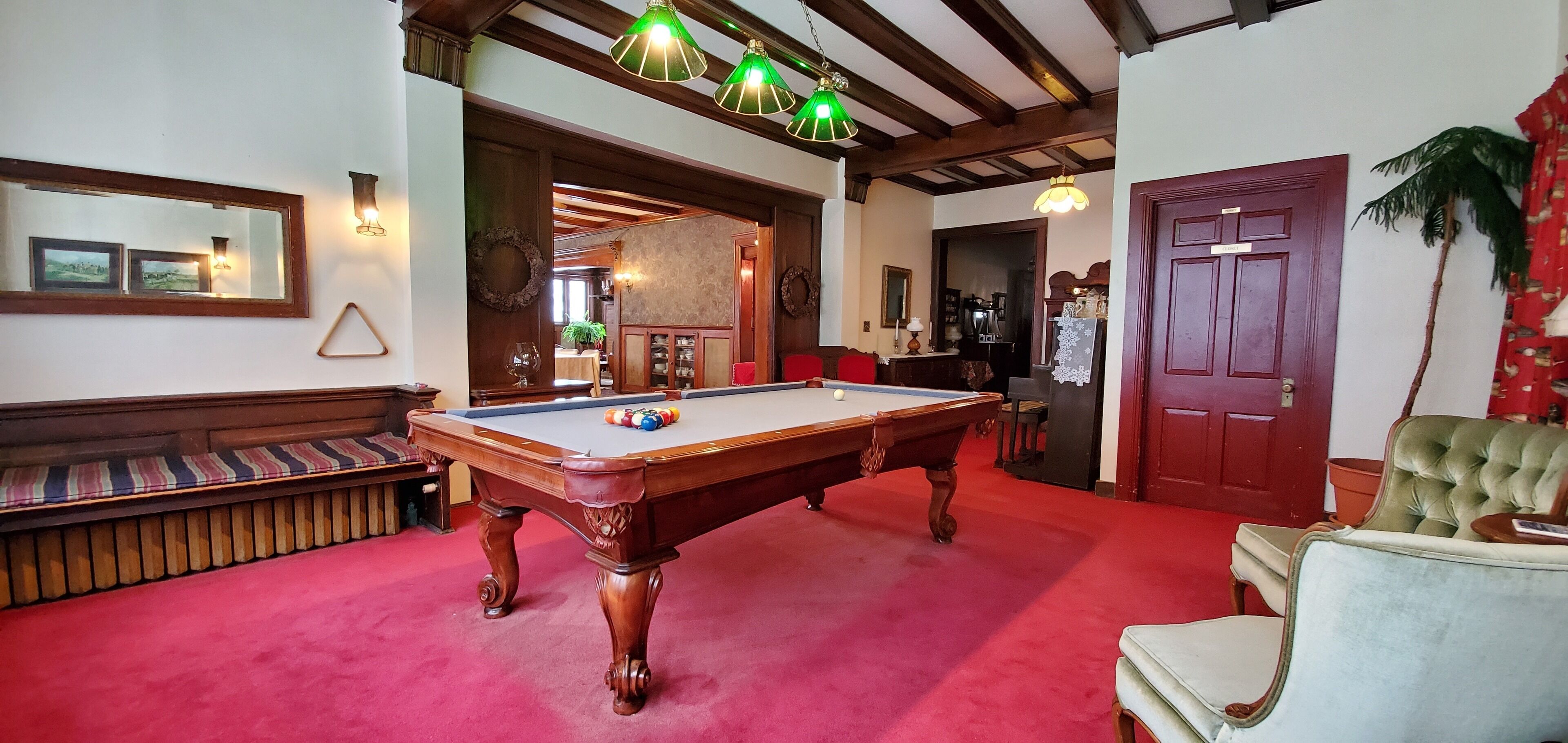 A billiards table with a red carpet, wooden benches, and a green armchair.
