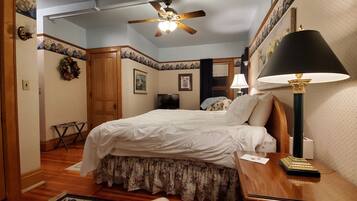 A bedroom with a bed, a ceiling fan, a nightstand with a lamp, and a door.