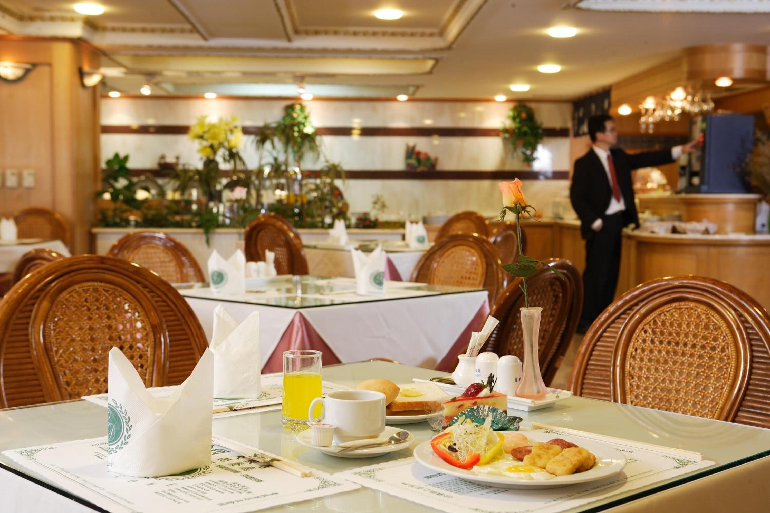 A dining area with tables set for breakfast, including plates of food, a glass of orange juice, and a vase with a flower.