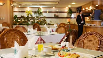 A dining area with tables set for breakfast, including plates of food, a glass of orange juice, and a vase with a flower.