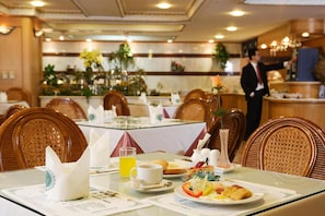 A dining area with tables set for breakfast, including plates of food, a glass of orange juice, and a vase with a flower. - Kingdom Hotel (Hsinchu)