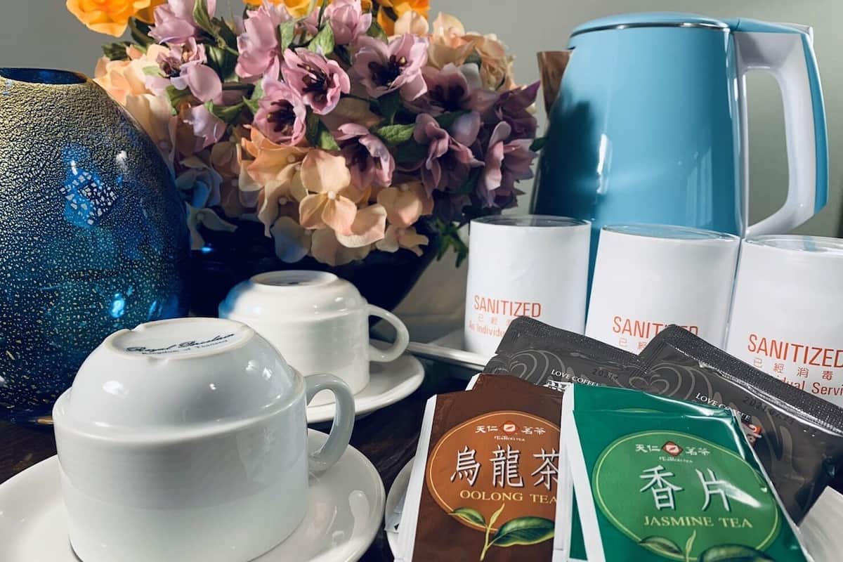 A table with a white cup, a blue pitcher, a vase with flowers, and several packets of tea.