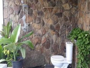 A bathroom with a stone wall, a toilet, and a potted plant. - Apichada Villa (Ko Pha-ngan)