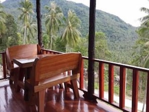 A wooden deck with a table and chairs overlooking a mountainous landscape with palm trees. - Apichada Villa (Ko Pha-ngan)