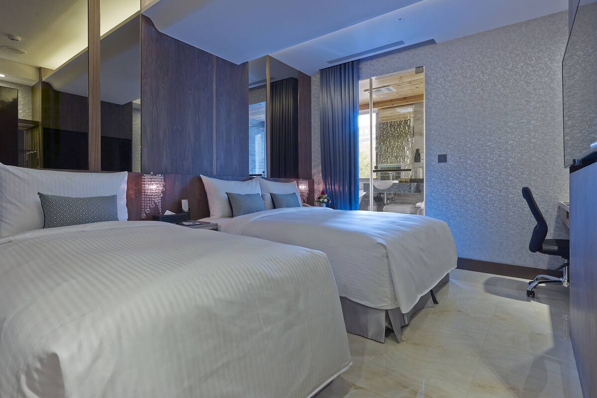 Una habitación de hotel moderna con dos camas grandes, un baño con lavamanos y espejo, y vistas al exterior.