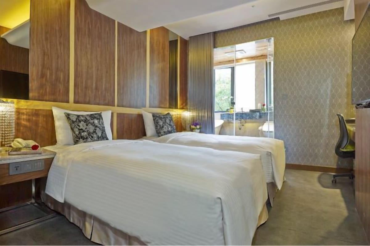 A hotel room with two beds, a desk with a telephone, a chair, and a large window.