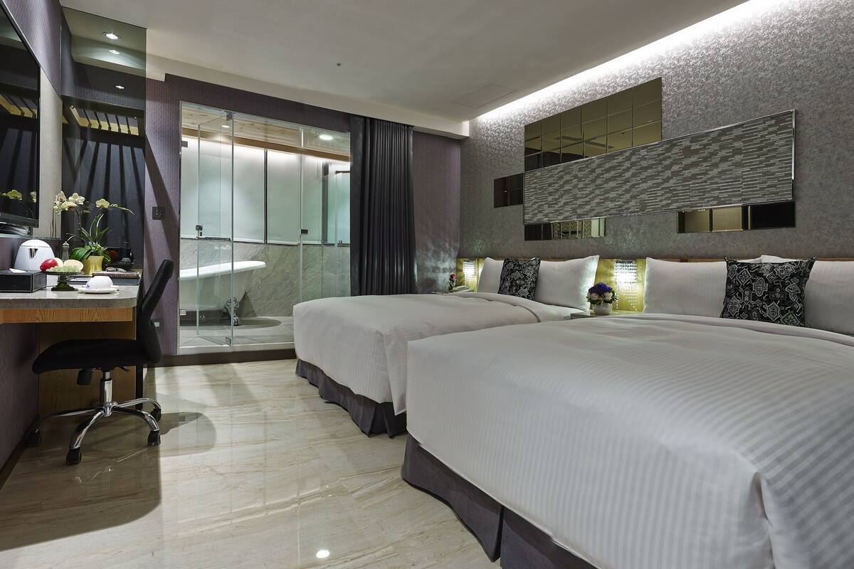 Una habitación de hotel moderna con dos camas, un escritorio y zona de ducha.