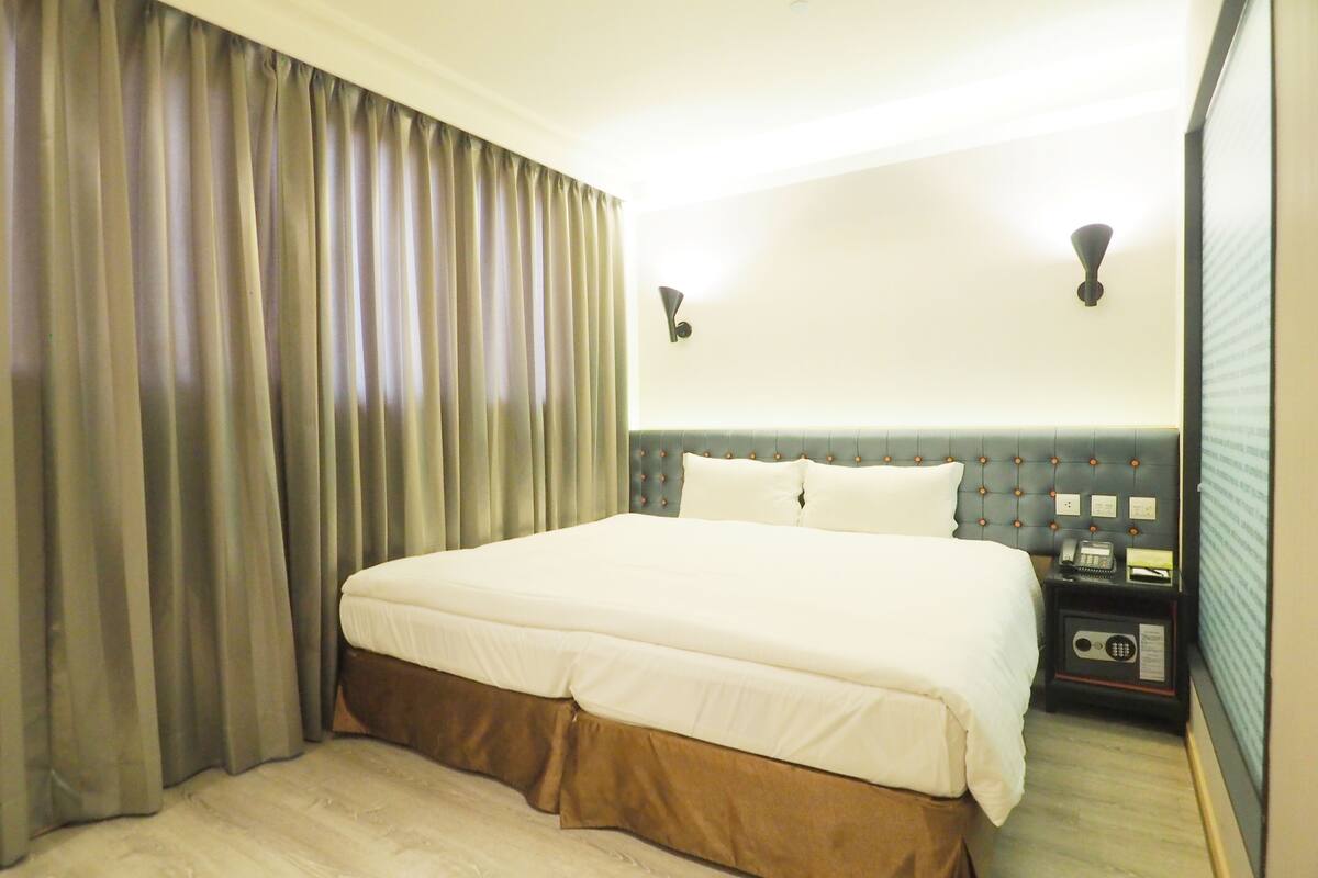 Una habitación de hotel con una cama grande, una mesita de noche con teléfono y una ventana con cortinas.