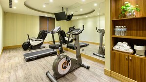 Un gimnasio con máquinas de cardio, un televisor y un estante de madera con toallas y botellas de agua.