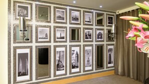 Una pared con fotografías en blanco y negro enmarcadas de monumentos famosos, un espejo y un jarrón con flores.