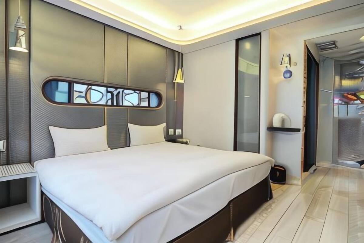 Una habitación de hotel moderna con una cama grande, una mesita de noche, una lámpara de pared y un armario.