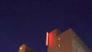 Un hôtel à plusieurs étages, reconnaissable à son grand panneau rouge placé à l’angle de la rue, à son entrée bien éclairée et à son parking situé devant.