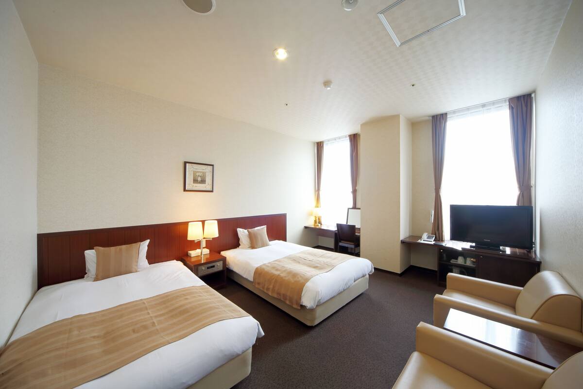 A hotel room with two beds, a TV, a desk, and a chair.