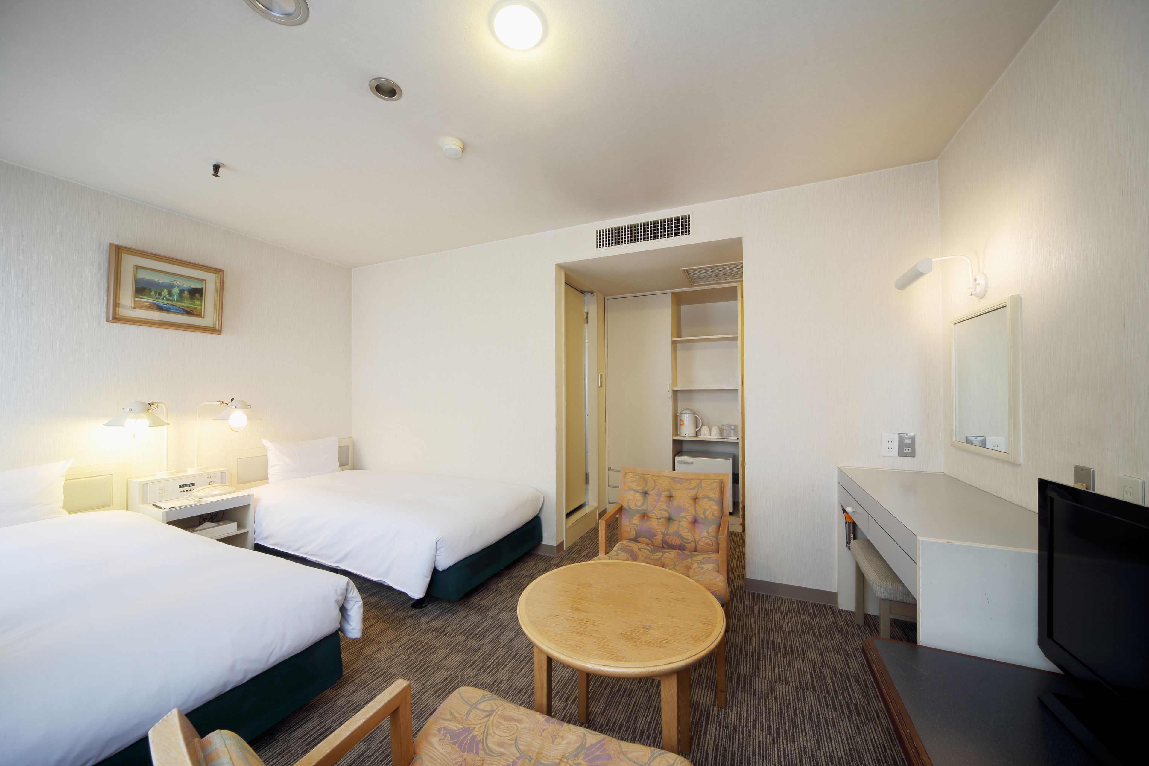 A hotel room with two beds, a desk, a chair, a television, and a small table.