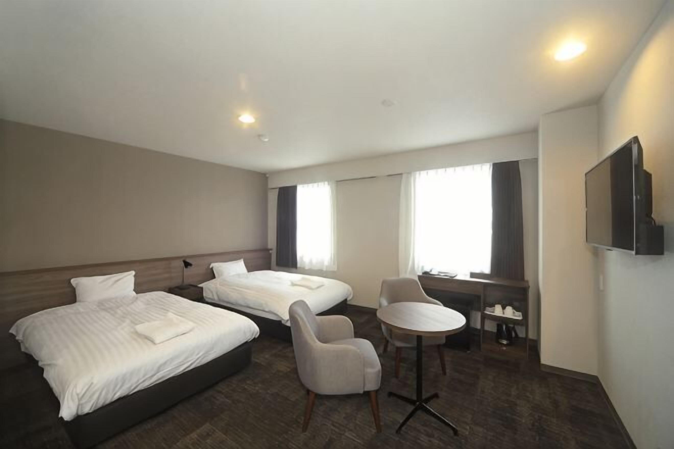 Een hotelkamer met twee bedden, een bureau, een stoel, een televisie en grote ramen.