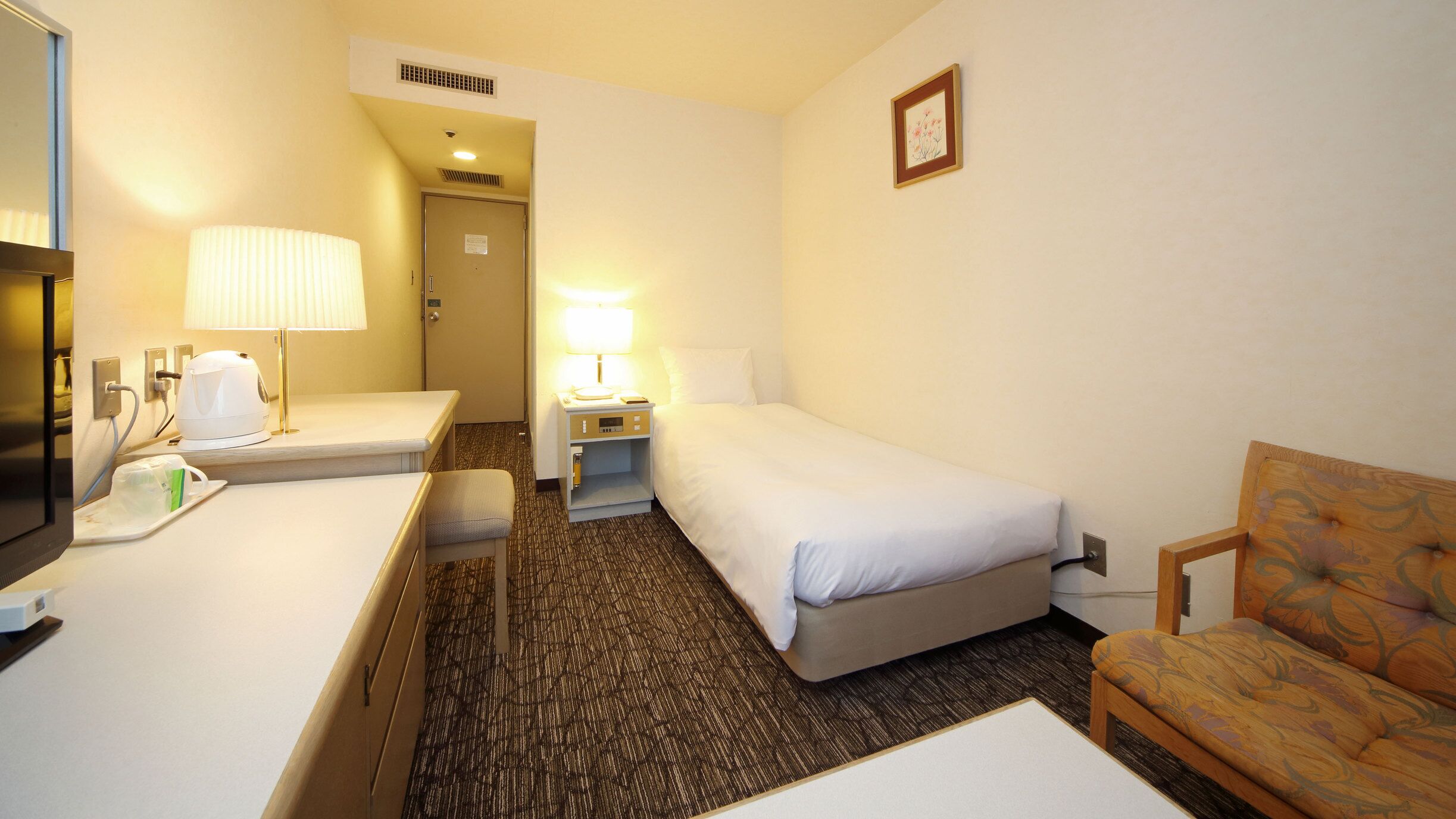 Een hotelkamer met een bed, een bureau met lamp, een stoel en een televisie.