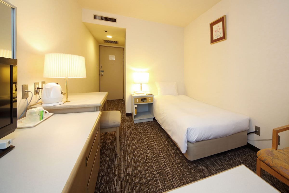 Une chambre d’hôtel avec un lit, un bureau avec une lampe, une chaise et un téléviseur.