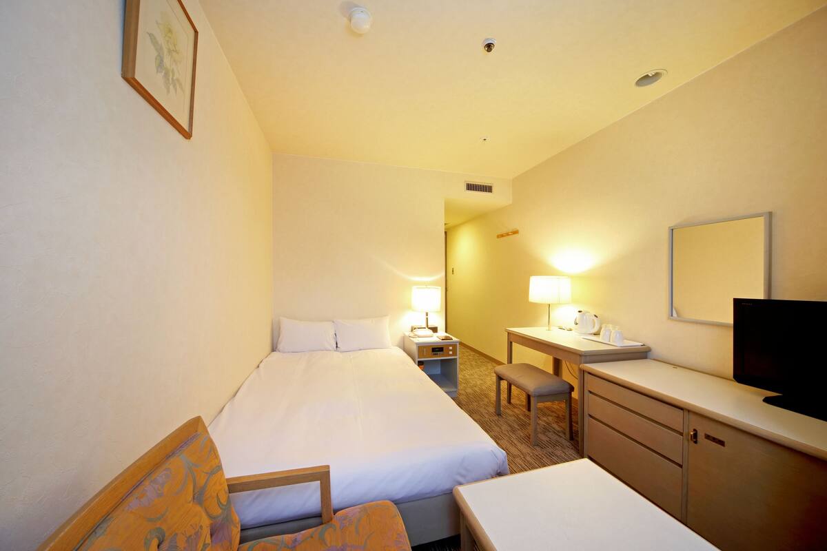 A hotel room with a bed, a desk, a chair, a TV, and a small table.