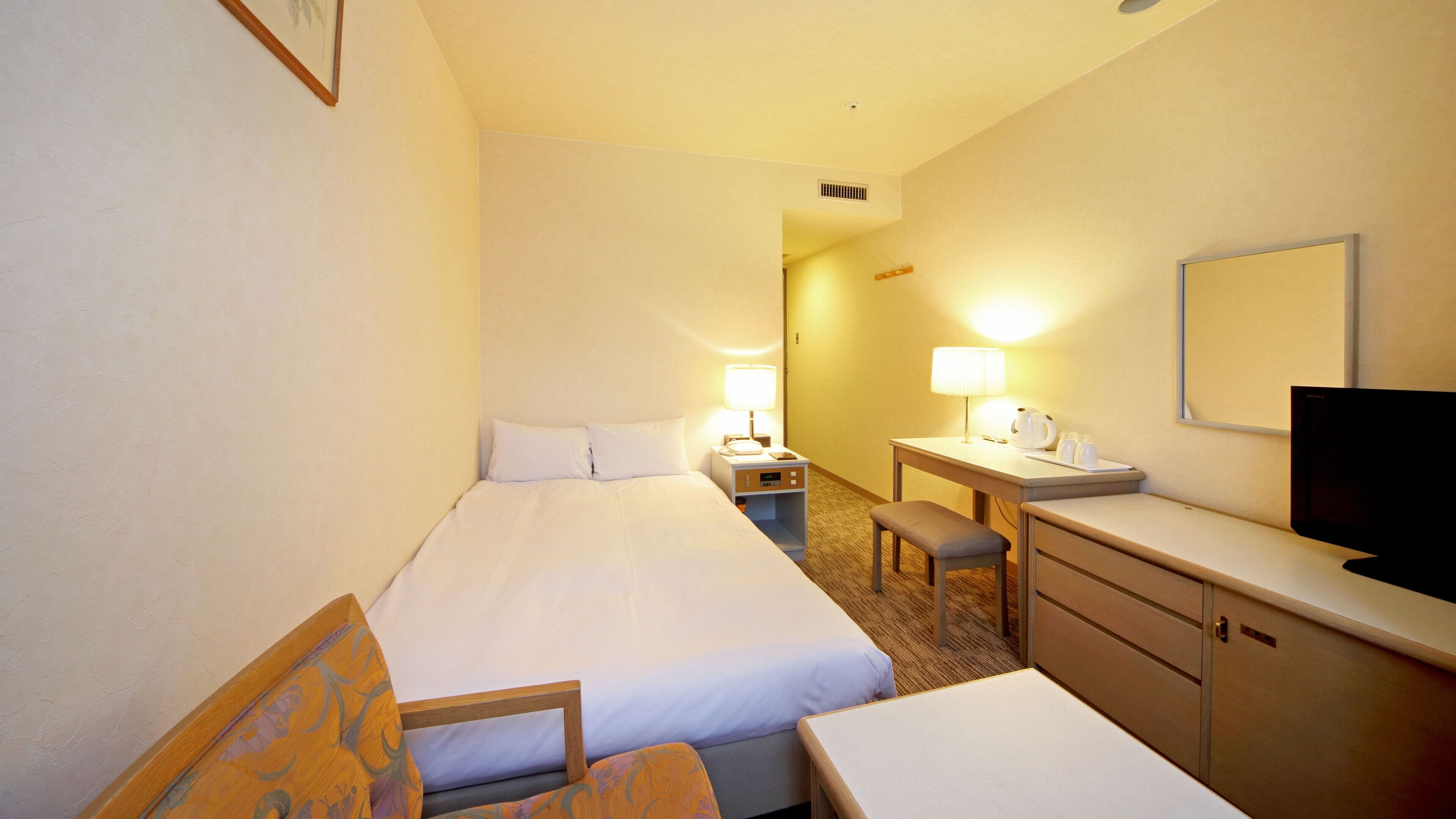 A hotel room with a bed, a desk, a chair, a television, and a nightstand with a lamp.