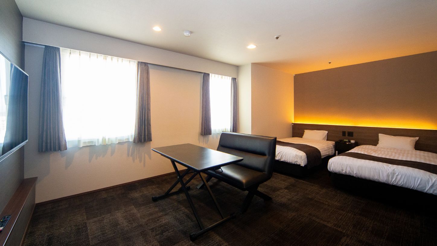 Een hotelkamer met een bed, een bureau, een stoel, een televisie en een groot raam met gordijnen.
