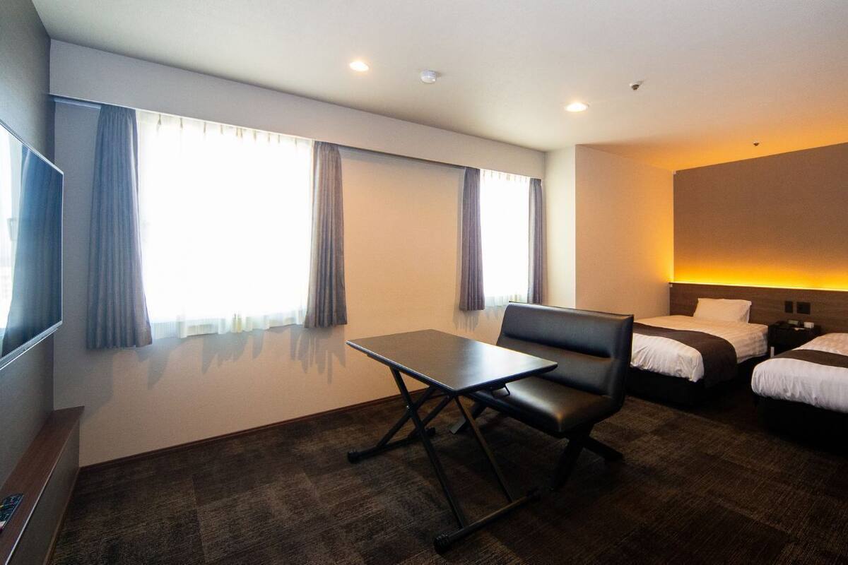 A hotel room with a bed, a desk, a chair, a TV, and a large window with curtains.
