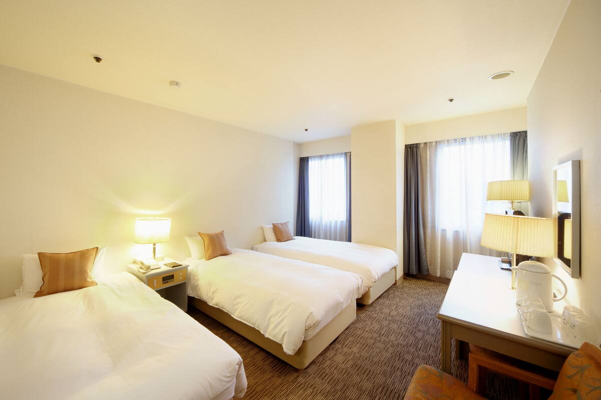 A hotel room with two beds, a desk, a chair, a lamp, and a coffee maker.
