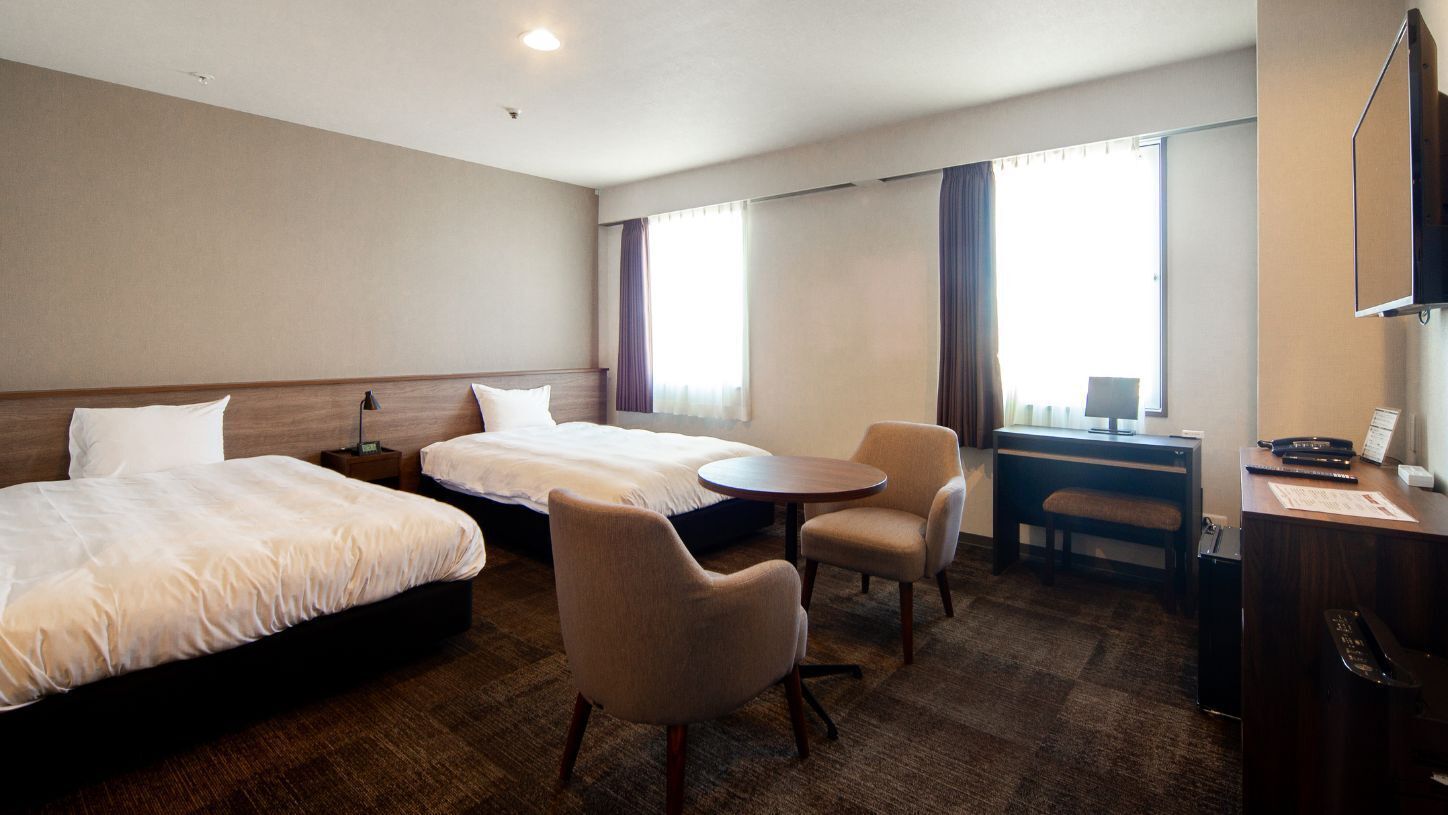 Een hotelkamer met twee bedden, een bureau, een stoel en een klein tafeltje.