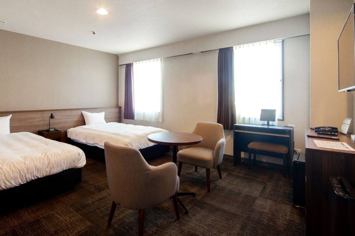 A hotel room with two beds, a desk, a chair, and a small table.