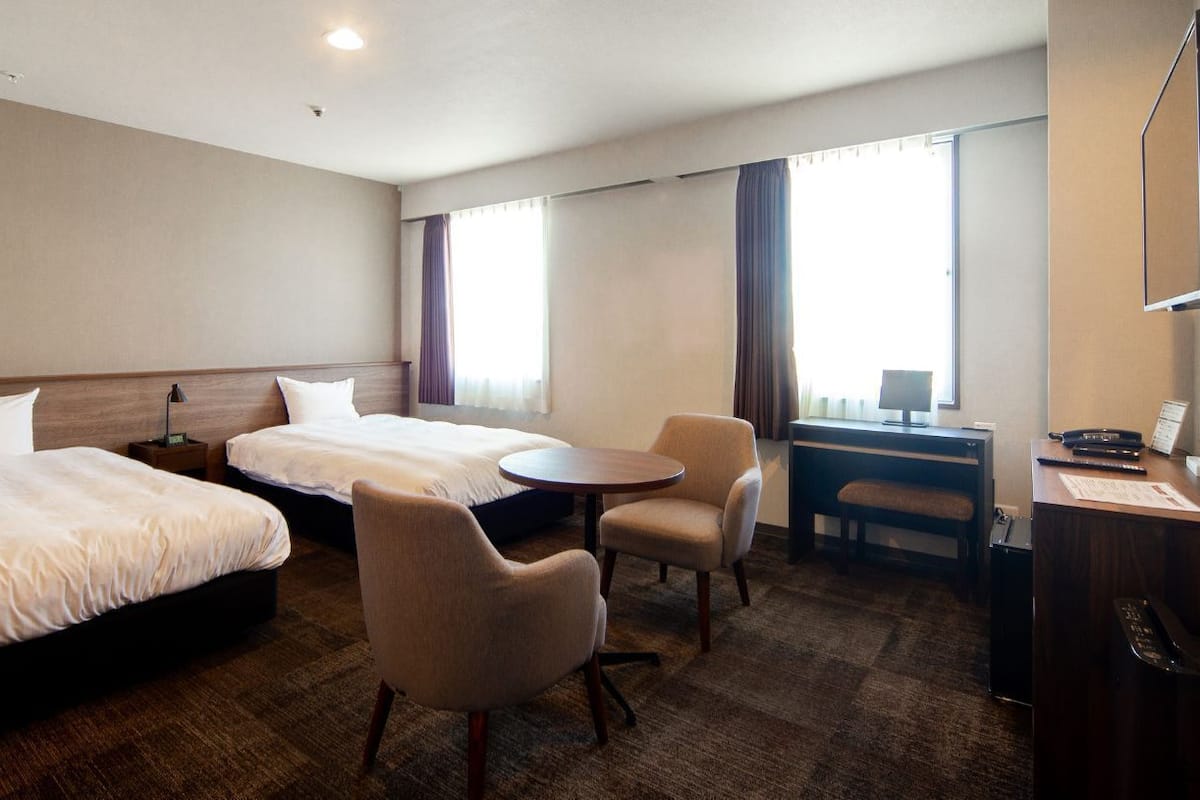 Une chambre d’hôtel avec deux lits, un bureau, une chaise et une petite table.