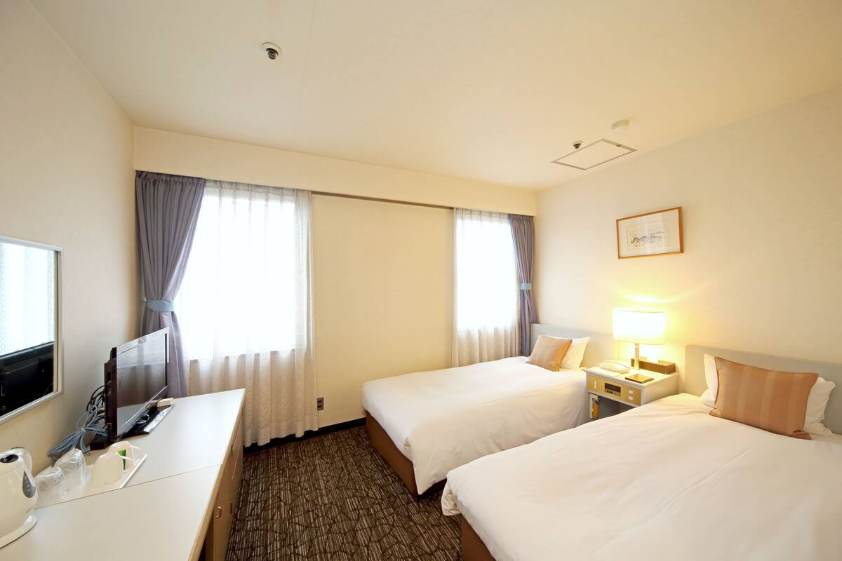 A hotel room with two beds, a desk, a TV, and a lamp.