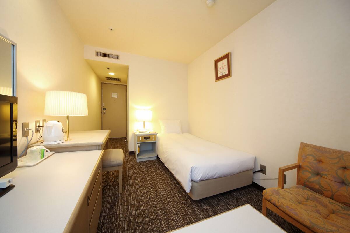 A hotel room with a bed, a desk with a lamp, a chair, and a television.