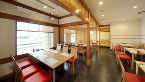 Une salle de conférence dotée de tables en bois et de chaises rouges, de grandes fenêtres et d’un plafond haut avec des poutres en bois.