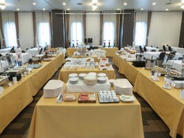 Une salle de conférence équipée de plusieurs tables aménagées pour un buffet, avec différents stands proposant une variété de plats et de boissons.