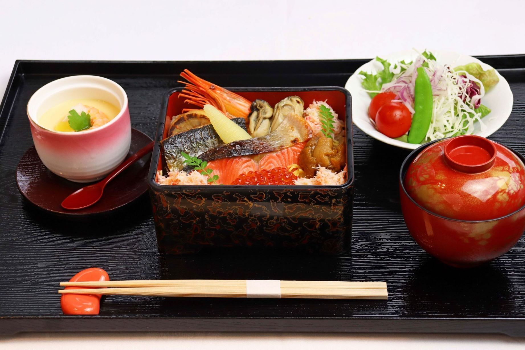 Eine traditionelle japanische Mahlzeit mit roher Fischspeise, einer Suppenschüssel, einem kleinen Salat und einem kleinen Topf Suppe.
