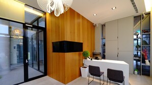 A reception desk with a wooden panel wall, a flat-screen TV, two chairs, and a potted plant.