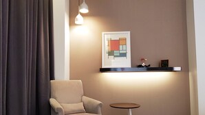 A modern room with a beige armchair, a small round table, and a framed abstract artwork on the wall.