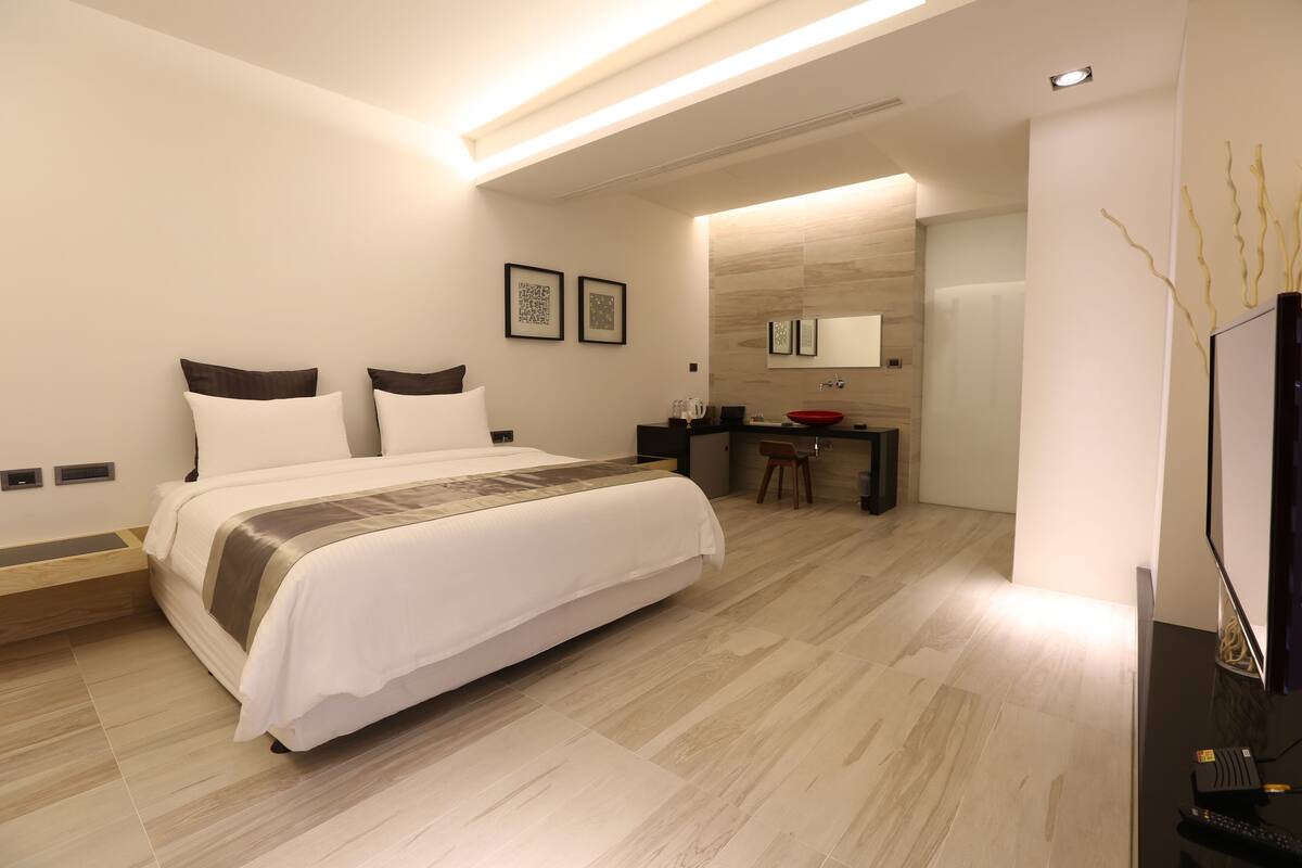 A modern hotel room with a large bed, a desk with a sink, and a television.