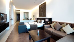A modern living room with a sofa, coffee table, and a TV. There is a bed with a nightstand and lamp. A decorative wall piece is above the bed. - Crystal Blue Boutique Hotel (Phnom Penh)