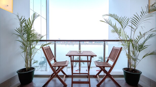 A balcony with a wooden table and two chairs, surrounded by potted plants, overlooking a body of water. - Crystal Blue Boutique Hotel (Phnom Penh)
