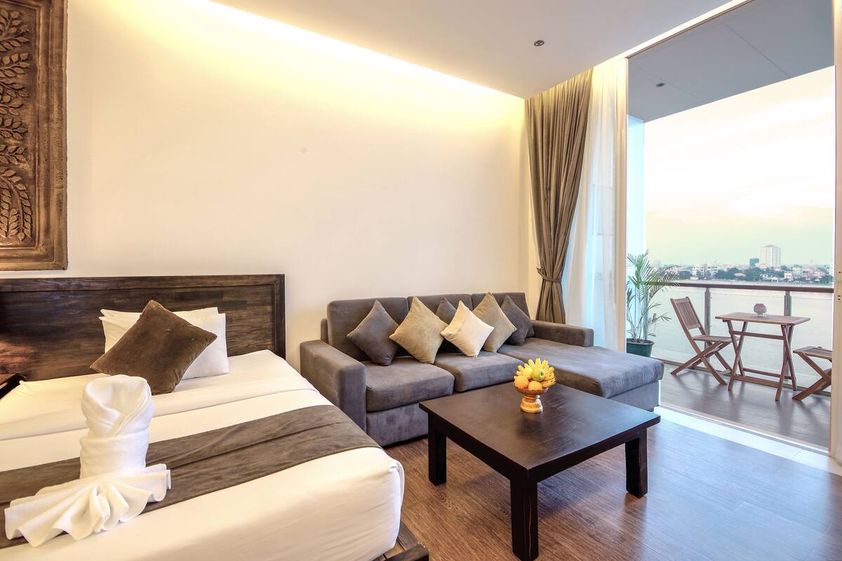 Habitación de hotel con cama, sofá, mesa de centro y balcón con vistas a la ciudad.
